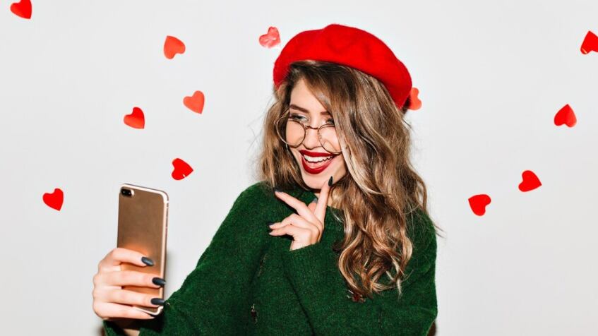 Mujer riendo con hermoso peinado haciendo selfie con corazones en la pared