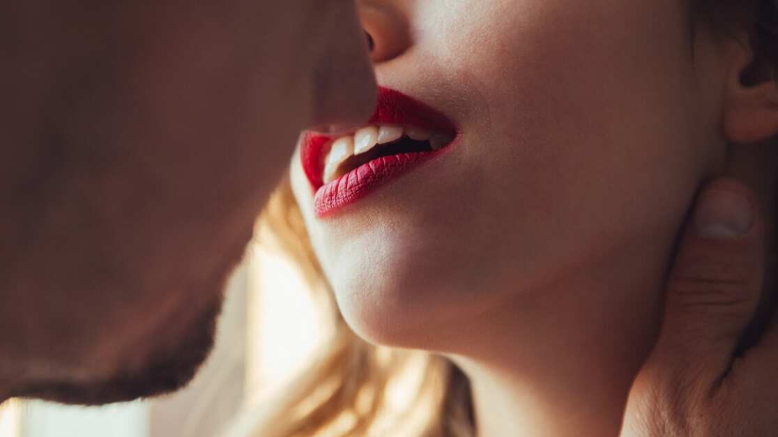 Foto recortada de jóvenes amantes besándose cerca de la ventana en casa.