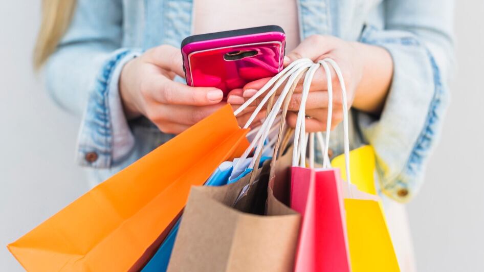 Mujer con brillantes bolsas de compras utilizando teléfono inteligente